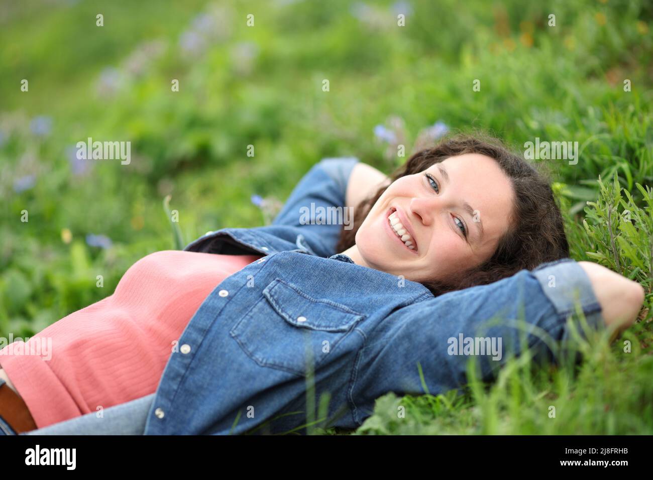 Glückliche Frau, die sich entspannt auf dem Gras liegend und in einem Park auf die Kamera schaut Stockfoto