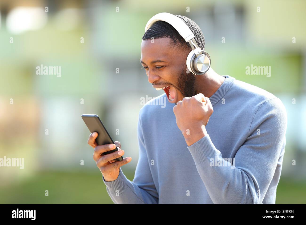 Aufgeregter Mann mit schwarzer Haut, der Musik auf dem Smartphone überprüft und auf der Straße feiert Stockfoto