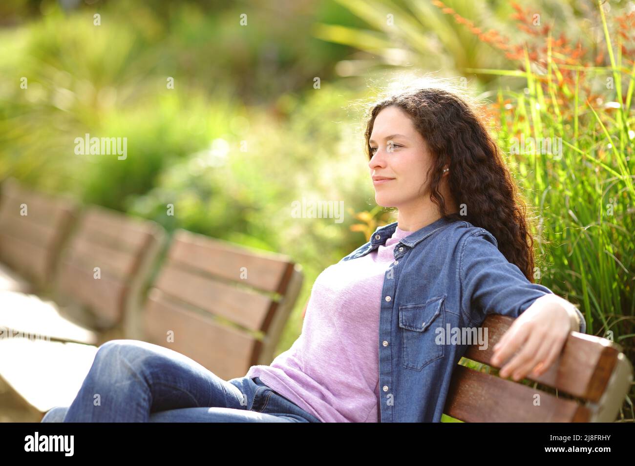 Entspannte Frau, die von einer Bank in einem Park aus die Aussicht betrachtet Stockfoto