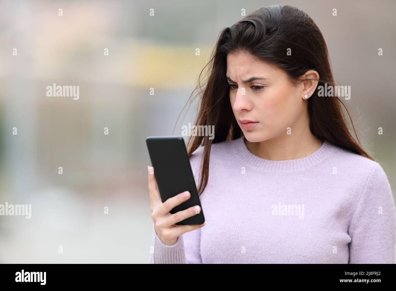 Besorgte Frau beim Lesen von Smartphone-Inhalten auf der Straße Stockfoto
