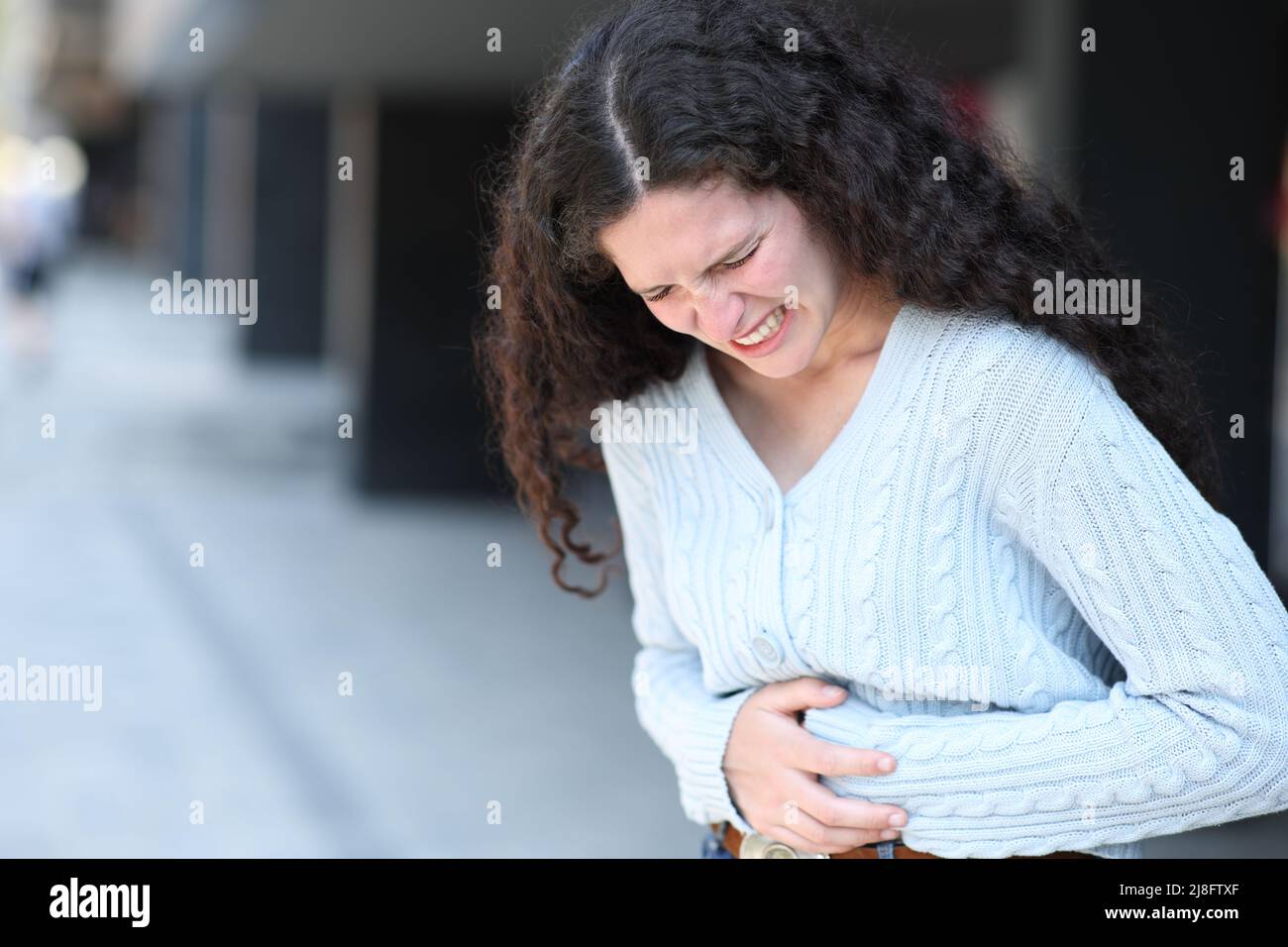 Gestresste Frau, die sich auf der Straße beschwert und Bauchschmerzen leidet Stockfoto