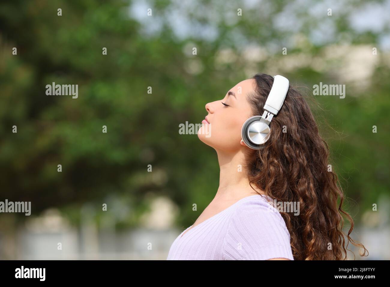 Seitenansicht Porträt einer entspannten Frau, die Kopfhörer trägt und Hörbücher in einem Park meditiert Stockfoto