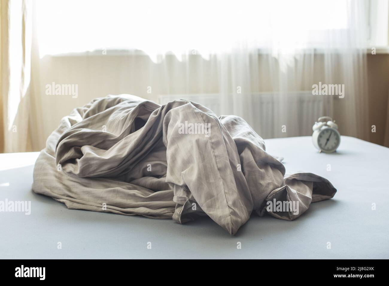 Zerknittert leeres Bett in einem Zimmer auf einem Fensterhintergrund. Wochenende morgens, Einsamkeit. Chaotische Decke im Schlafzimmer nach dem Aufwachen Stockfoto