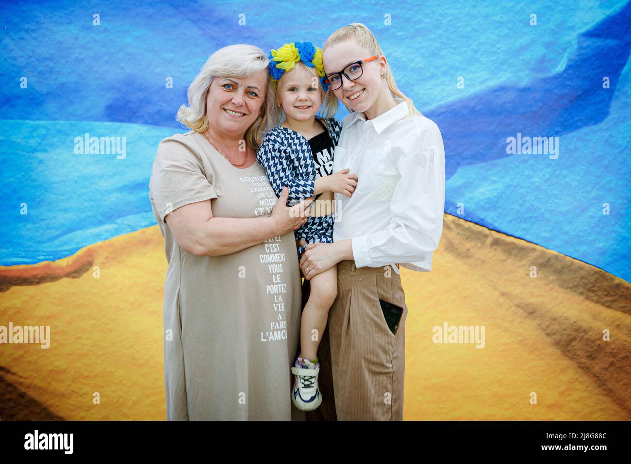 Zwei Frauen halten ein Mädchen fest, während lokale Fotografen vor dem Hintergrund der ukrainischen Flagge Porträts von Menschen machen, um Geld für das ukrainische Militär zu sammeln, Uschhorod, Region Zakarpattia, Westukraine, Mai 14, 2022. Foto von Serhii Hudak/Ulrinform/ABACAPRESS.COM Stockfoto