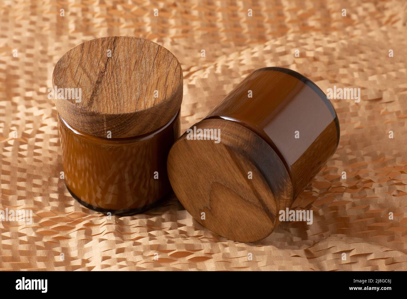 Behälter für Kosmetik und Cremes. Glas braun mit Holzdeckel. Beigefarbener Hintergrund. Monochromes Konzept. Für ein Etikett platzieren. Cremegläser. Schönheit und Pflege. Minimalismus Stockfoto