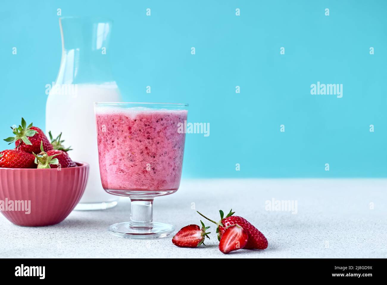 Erdbeer-Kokosnuss-Milchshake, Frappé oder Smoothie im Trinkglas auf hellblauem Hintergrund. Gesunde vegane Ernährung erfrischendes Getränk. Gesunde Ernährung und dri Stockfoto