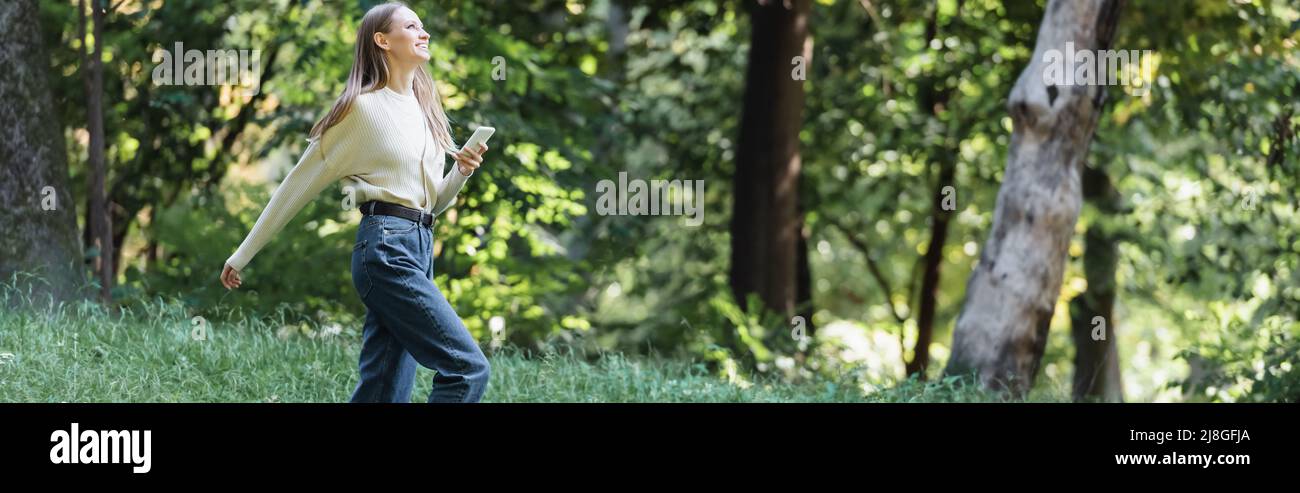 Glückliche junge Frau mit Smartphone im Park, Banner Stockfoto