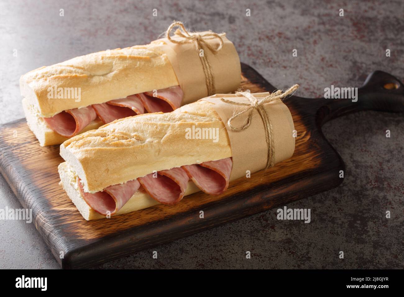 Jambon Beurre Französisch nationalen Sandwich gefüllt mit Jambon, Schinken, in einem Baguette in zwei Hälften geschnitten geschnitten und gefüllt mit Butter Nahaufnahme auf dem Holzschwein Stockfoto