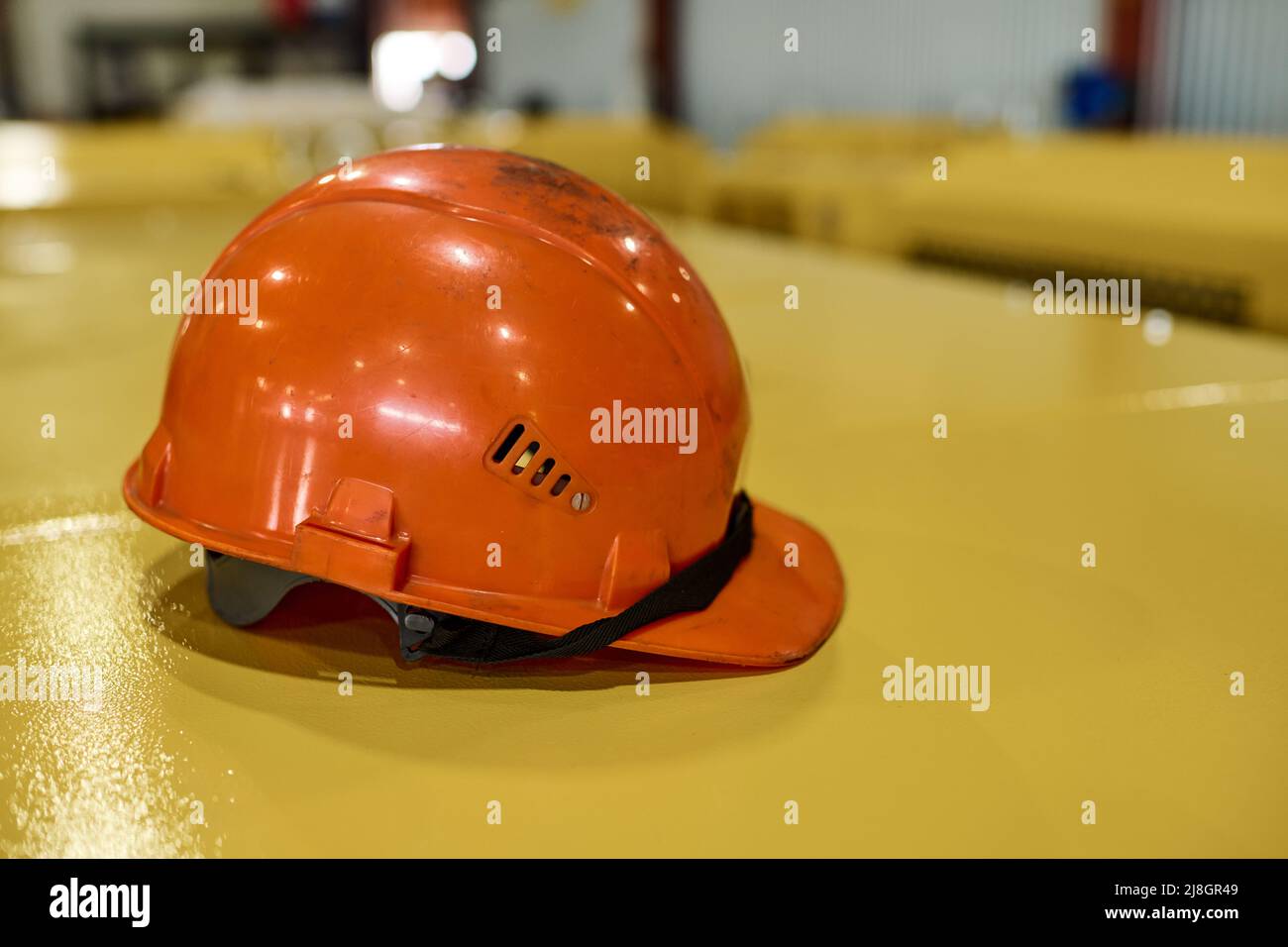 Schutzhelm der orangen Farbe auf gelber metallischer Abdeckung der industriellen Maschine oder anderer Ausrüstung innerhalb der Werkstatt der modernen Fabrik Stockfoto