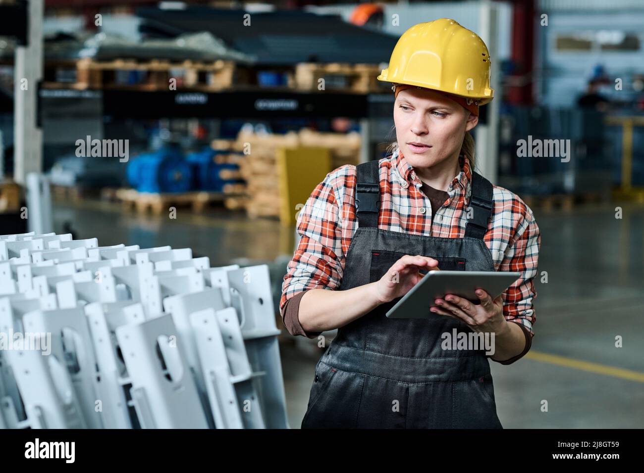 Junge Ingenieurin der modernen Fabrik mit Tablette, die die Qualität der neuen Industrieanlagen überprüft und Daten in die Datenbank eingibt Stockfoto