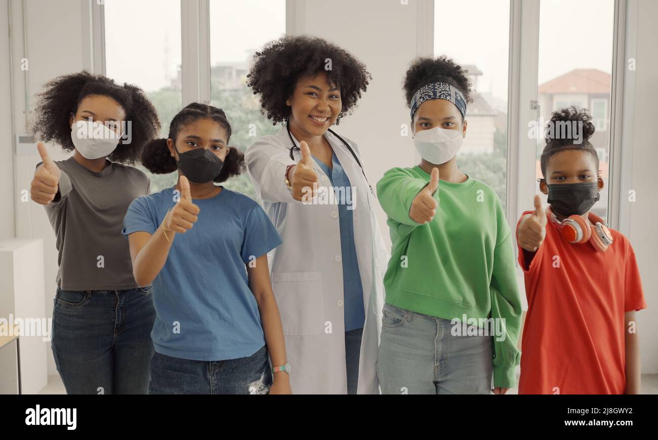 Afroamerikanischer Arzt und Kinder mit Maske glücklich Daumen nach oben Finger im Krankenhaus oder in der Klinik. Stockfoto