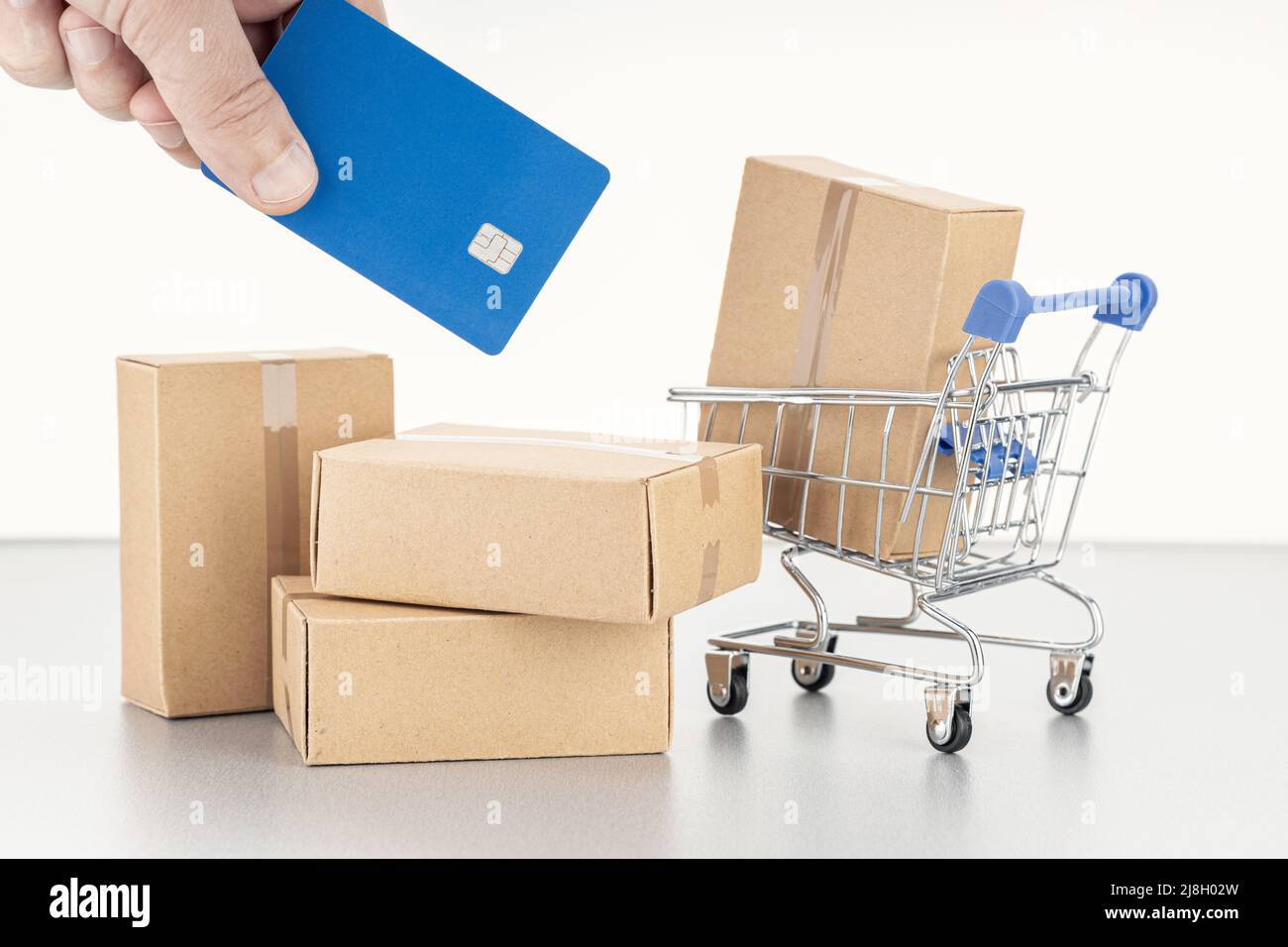 Shopping- oder Kaufkonzept mit Kreditkarte. Menschliche Hand mit Kreditkarte, leeren Kartons und Warenkorb Stockfoto