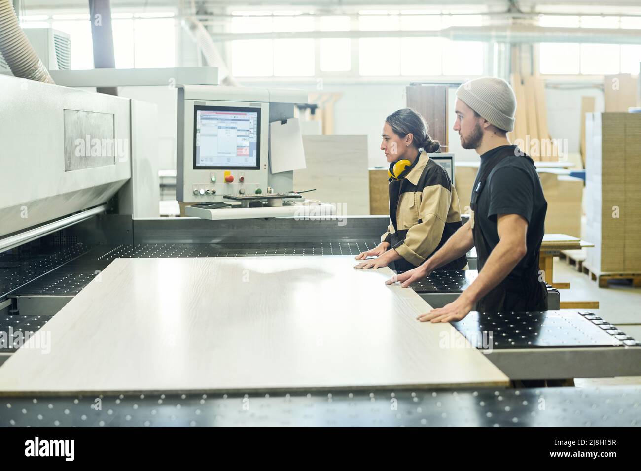 Zwei junge Kollegen setzen das große Holzbrett in der Fabrik auf die Schneidemaschine Stockfoto