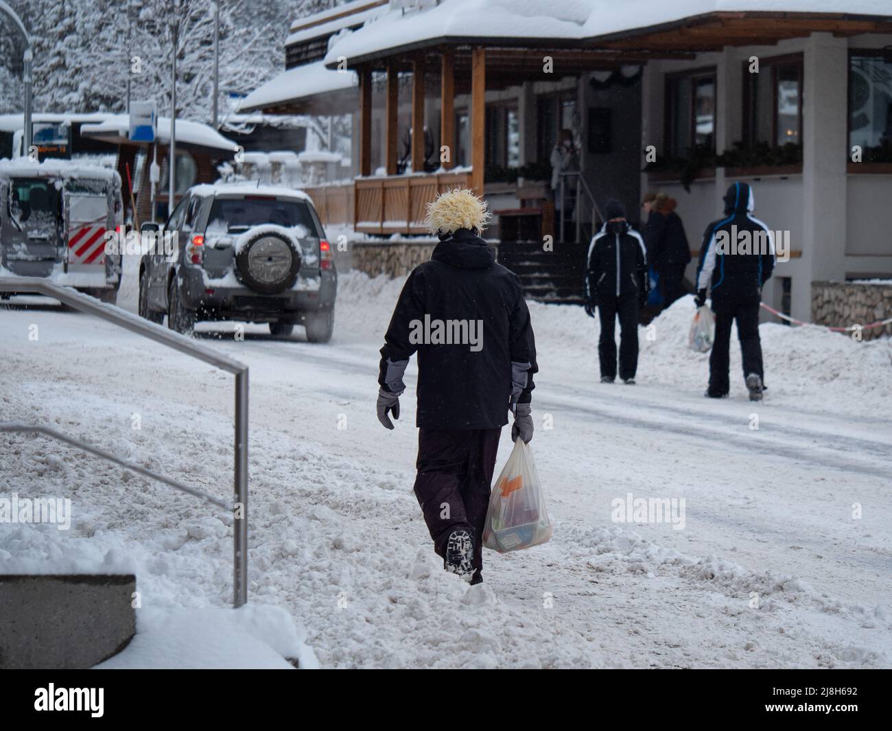 Skifahrer in Skianzügen gehen eine verschneite Straße mit Einkaufstüten in ihren Händen entlang. Stockfoto