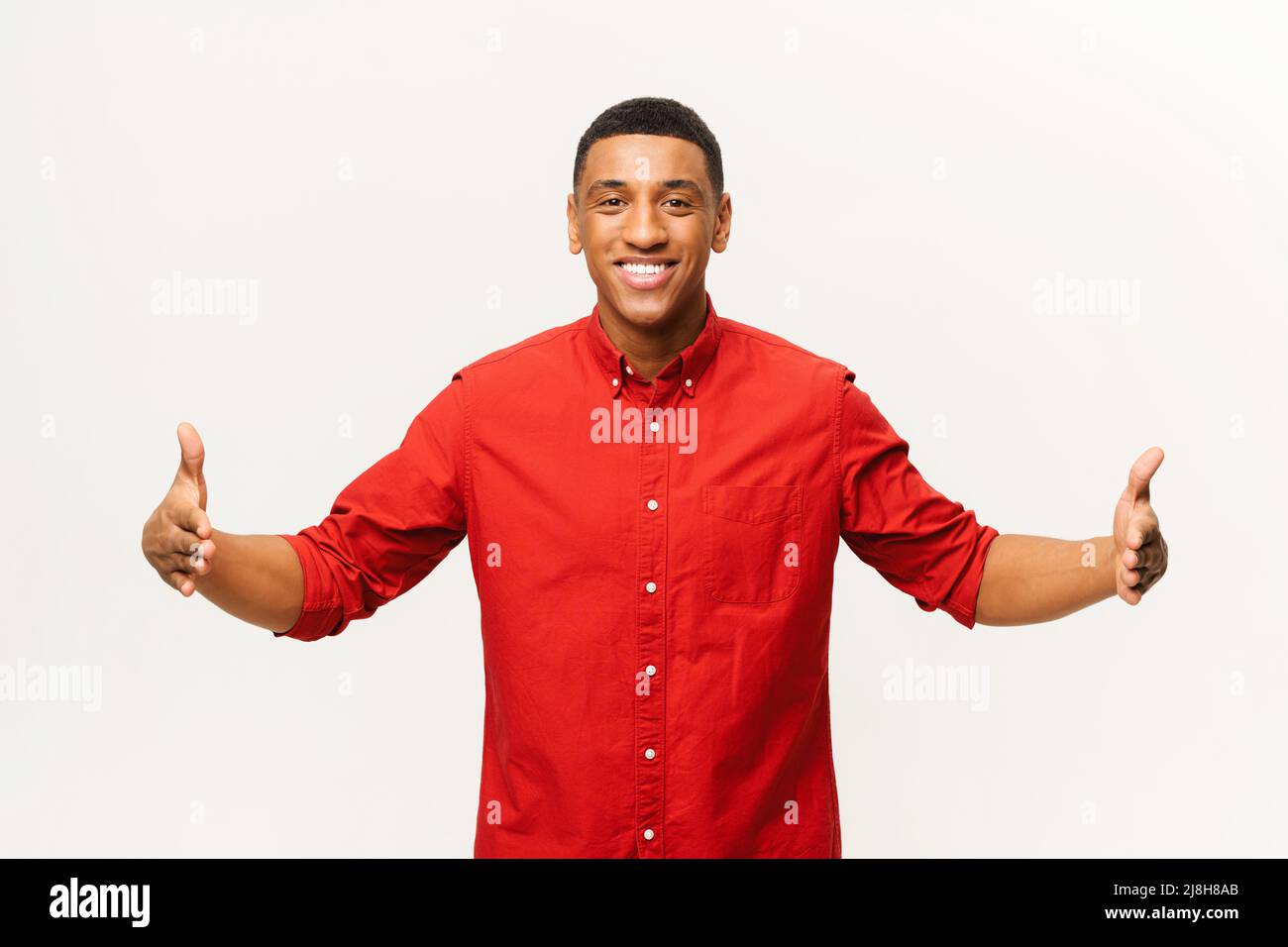 Fröhlicher Aferican-amerikanischer junger Mann, der zwei Hände vor sich hält und den großen, lateinischen Mann im roten Hemd zeigt, der Neuheit wirbt und ein Produkt auf weißem Hintergrund isoliert präsentiert Stockfoto