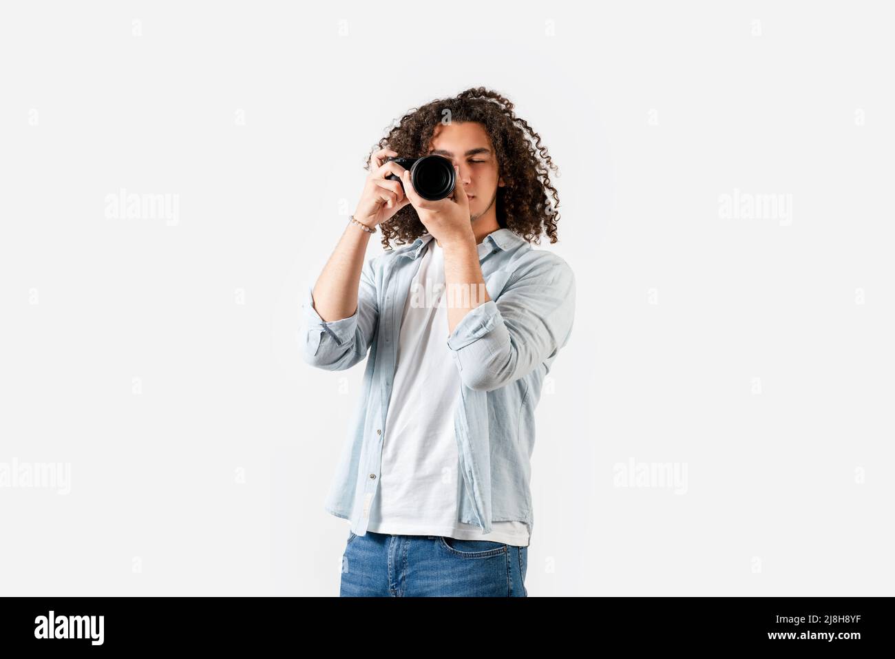 Der junge Mann mit lockigen Haaren schießt mit der Kamera an der Hand. Hobby und Fotografie Konzept. Hochwertige Fotos Stockfoto