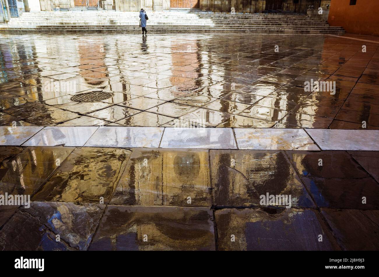 Granada, Andalusien, Spanien : Eine Frau geht auf der Spiegelung der Kathedrale auf dem nassen Bürgersteig des Platzes Plaza de las Pasiegas spazieren. Stockfoto