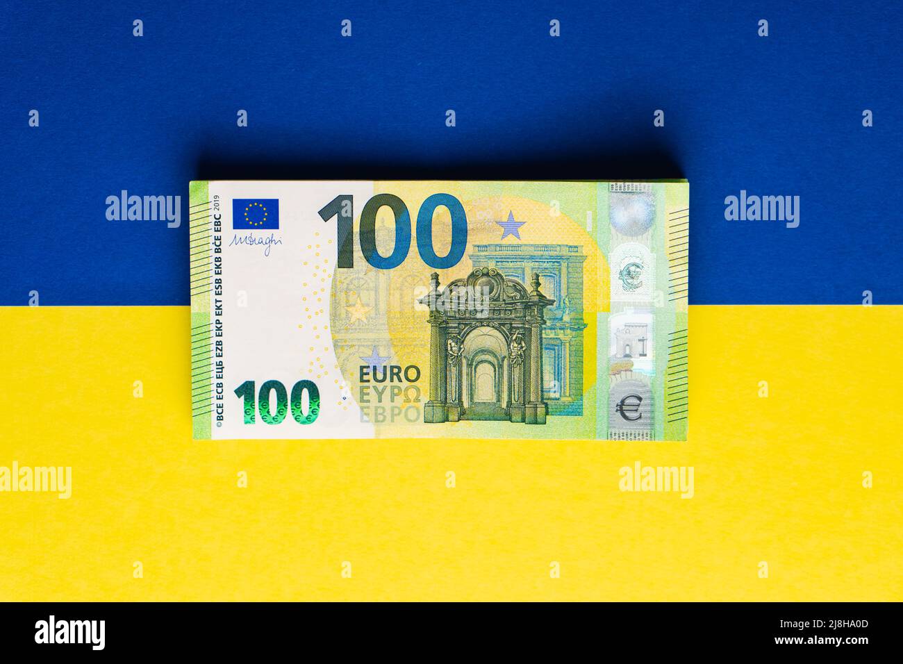 Stapel von hundert Euro-Banknoten auf ukrainischer Flagge. Geldhilfe aus Europa in die Ukraine Konzept Stockfoto