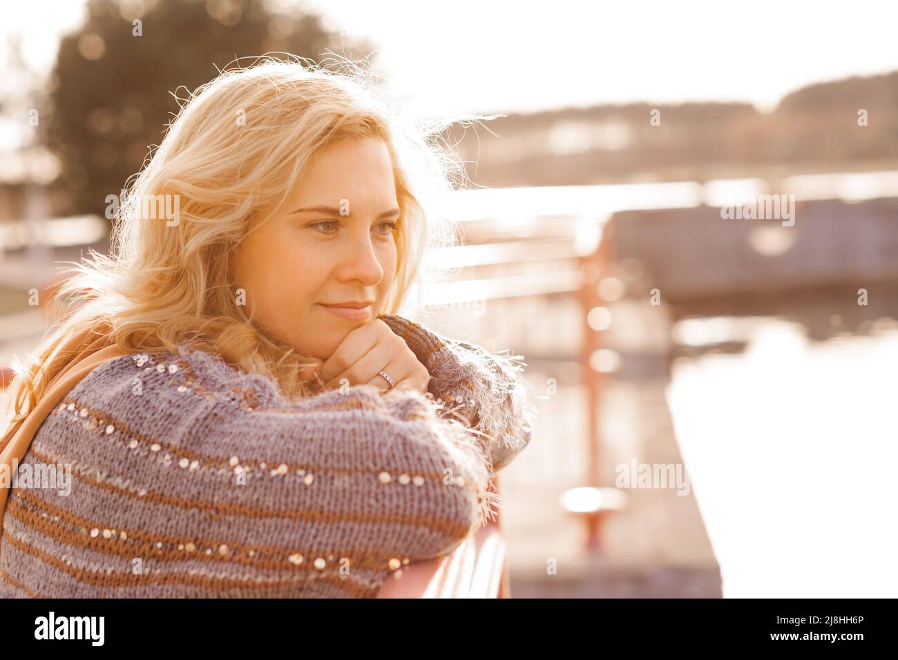 Nahaufnahme einer schönen blonden Frau, die an einem kühlen, sonnigen Tag auf dem Steg am Flussufer spazieren geht, sich entspannt, reflektiert und Frieden und Freiheit genießt Stockfoto