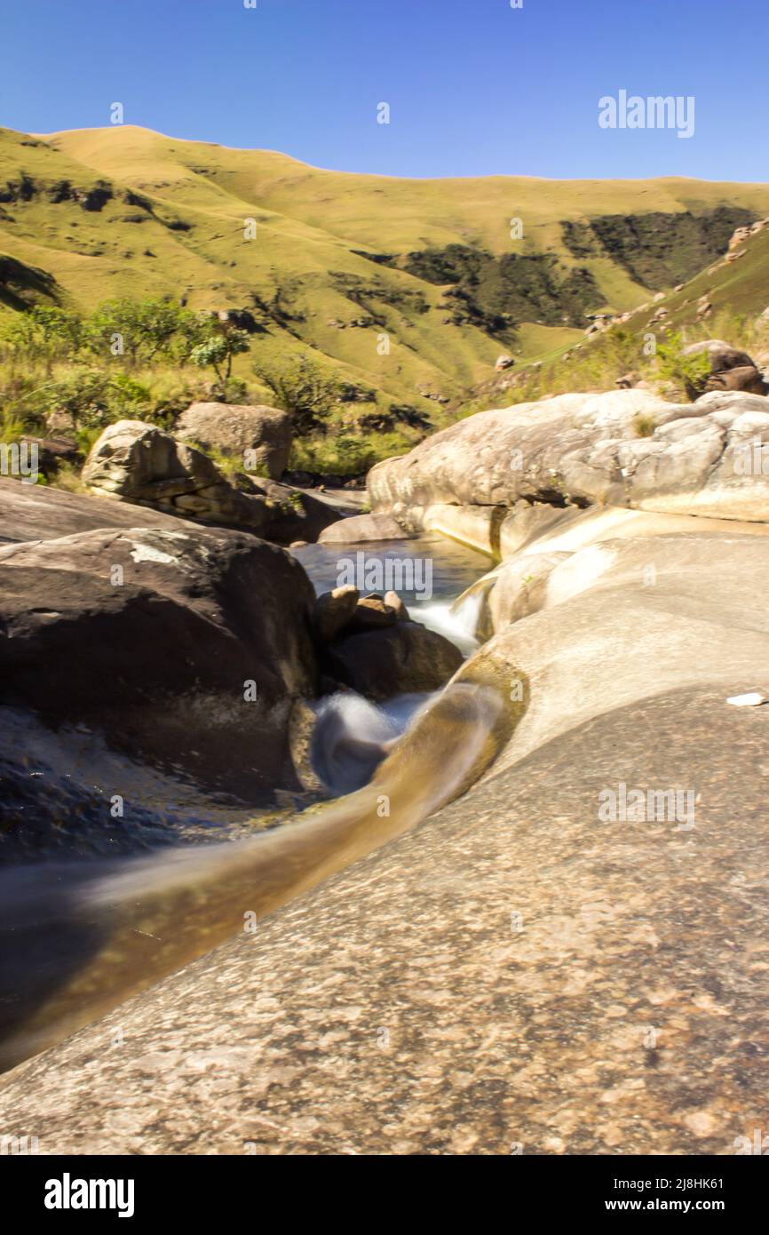 Langzeitbelichtung eines schnell fließenden Gebirgsstroms in den Drakensberg-Bergen Südafrikas an einem klaren, sonnigen Tag Stockfoto