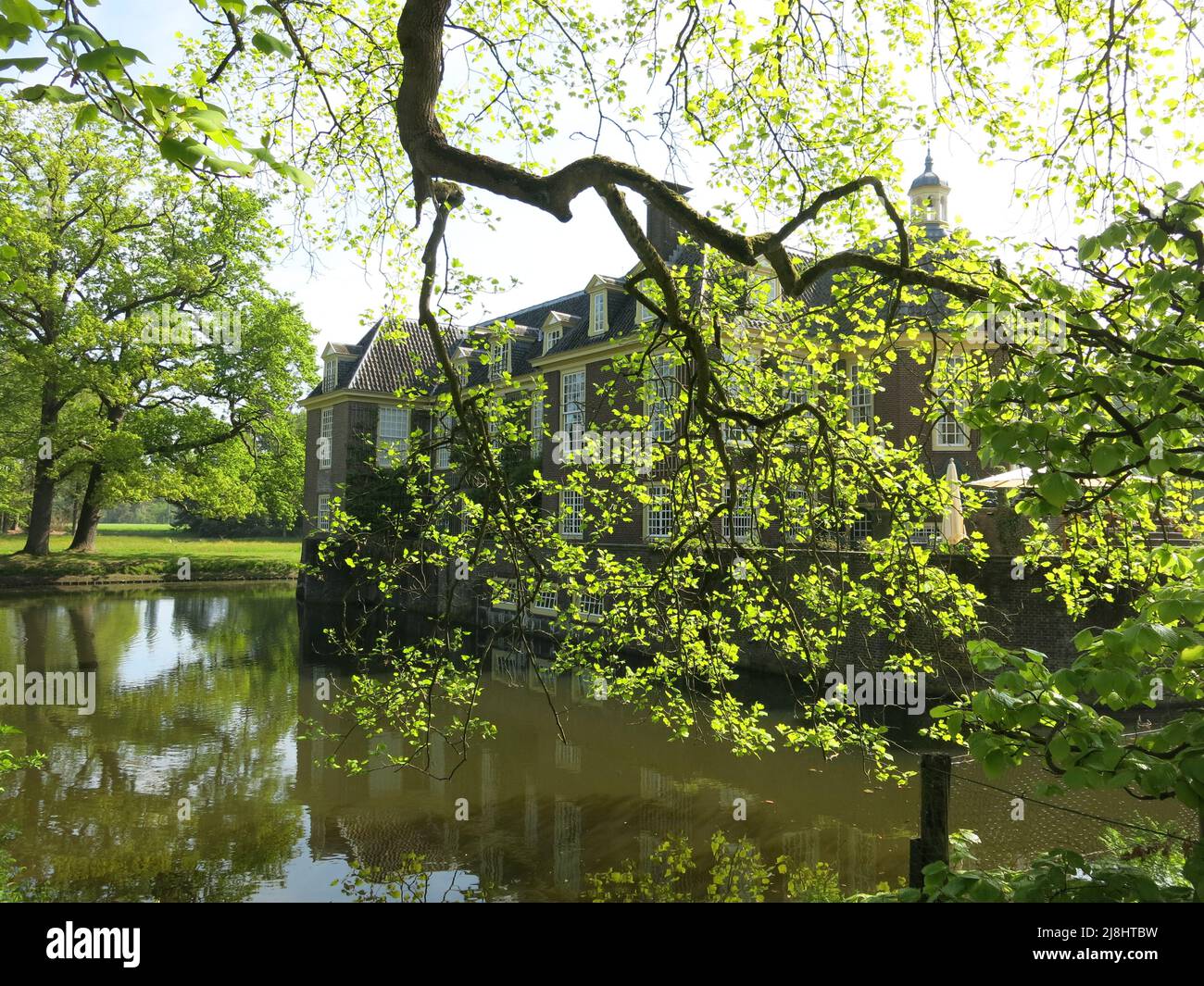 Blick auf das Wasserschloss von De Wiersse, von der anderen Seite des Baches mit strahlenden Sonnenstrahlen und Frühlingsbelaubung; Vorden, Niederlande, Mai 2022 Stockfoto