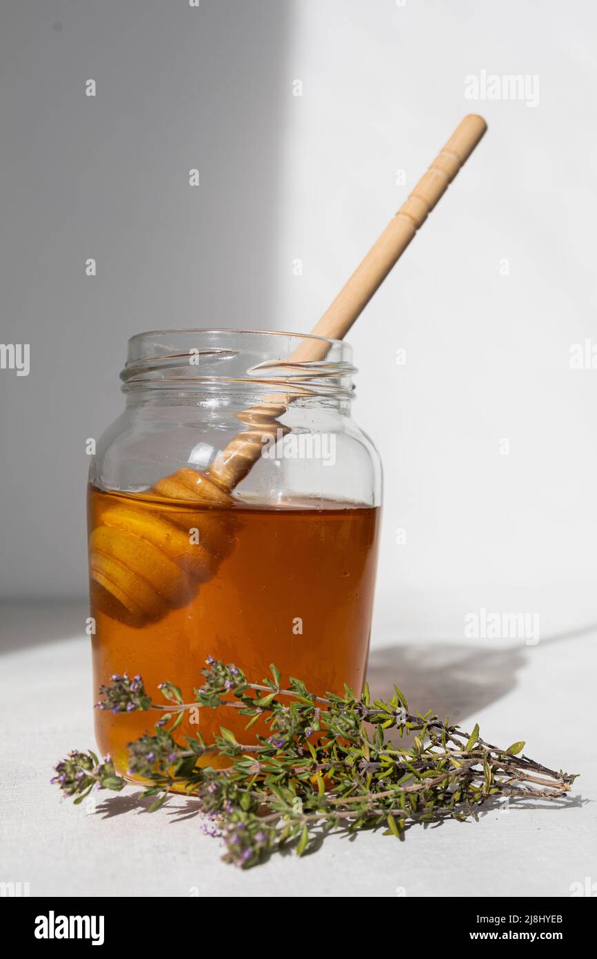 Glas mit rohem Honig von Bienen mit Honigtropfen und Honiglöffel Stockfoto