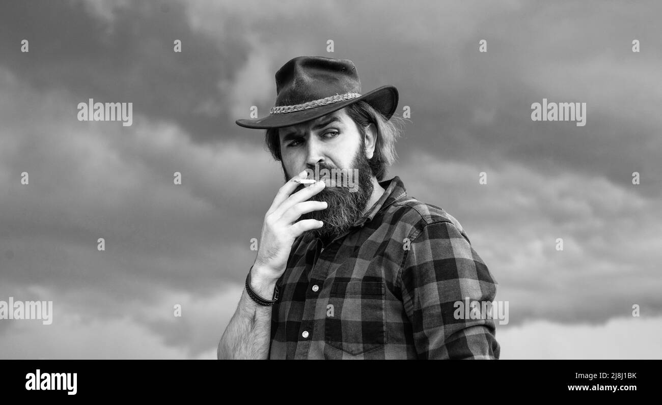 Reifer brutaler Hipster im Cowboyhut, der Zigarette raucht, schlechte Angewohnheit Stockfoto