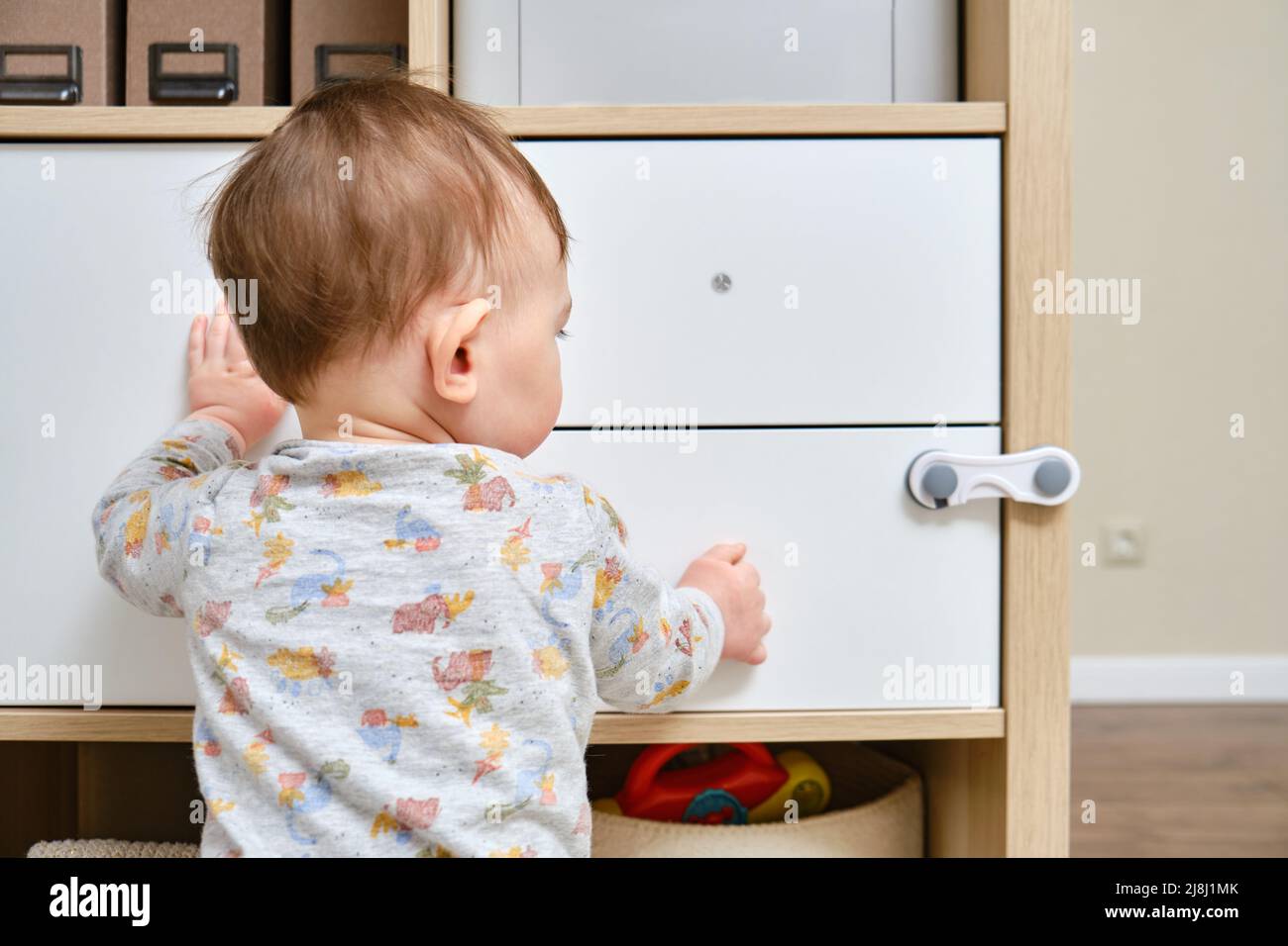 Kleinkind Baby Junge reißt aus einem Schrank Schublade mit seiner Hand. Das Kind hält den Schranktürgriff, kleines Kind Stockfoto