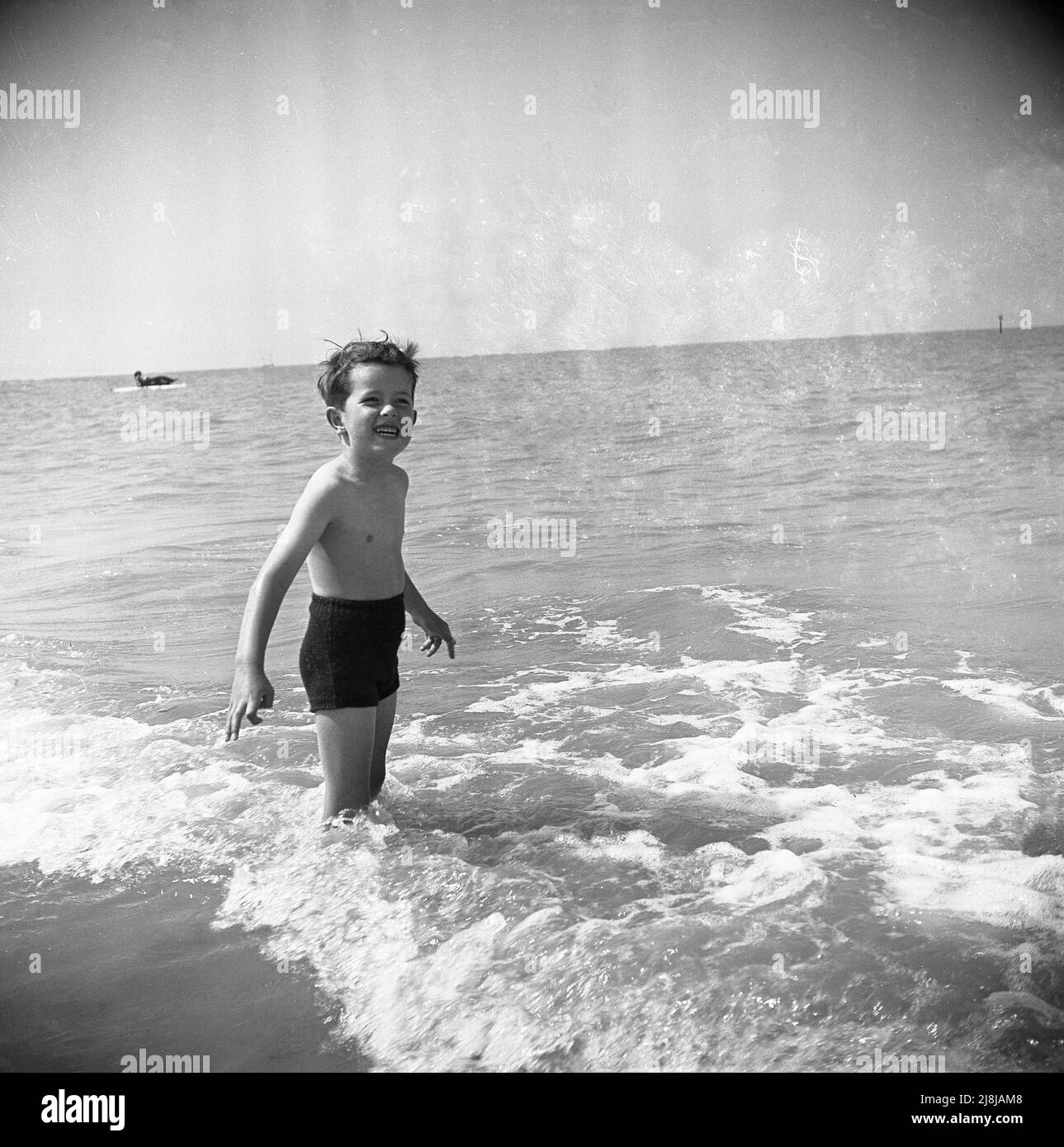 1950s, historisch, ein kleiner Junge in den wollenen Badehosen der Zeit, der im Wasser am Meeresrand stand, Margate, Kent, England, Großbritannien. Stockfoto