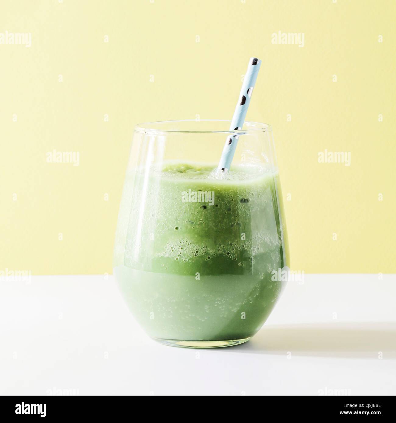 Gesunder grüner Smoothie im Glas mit Stroh auf gelbem Hintergrund. Vegetarisches gesundes Lifestyle-Konzept. Erfrischendes Getränk Quadrat. Schneller Snack Stockfoto