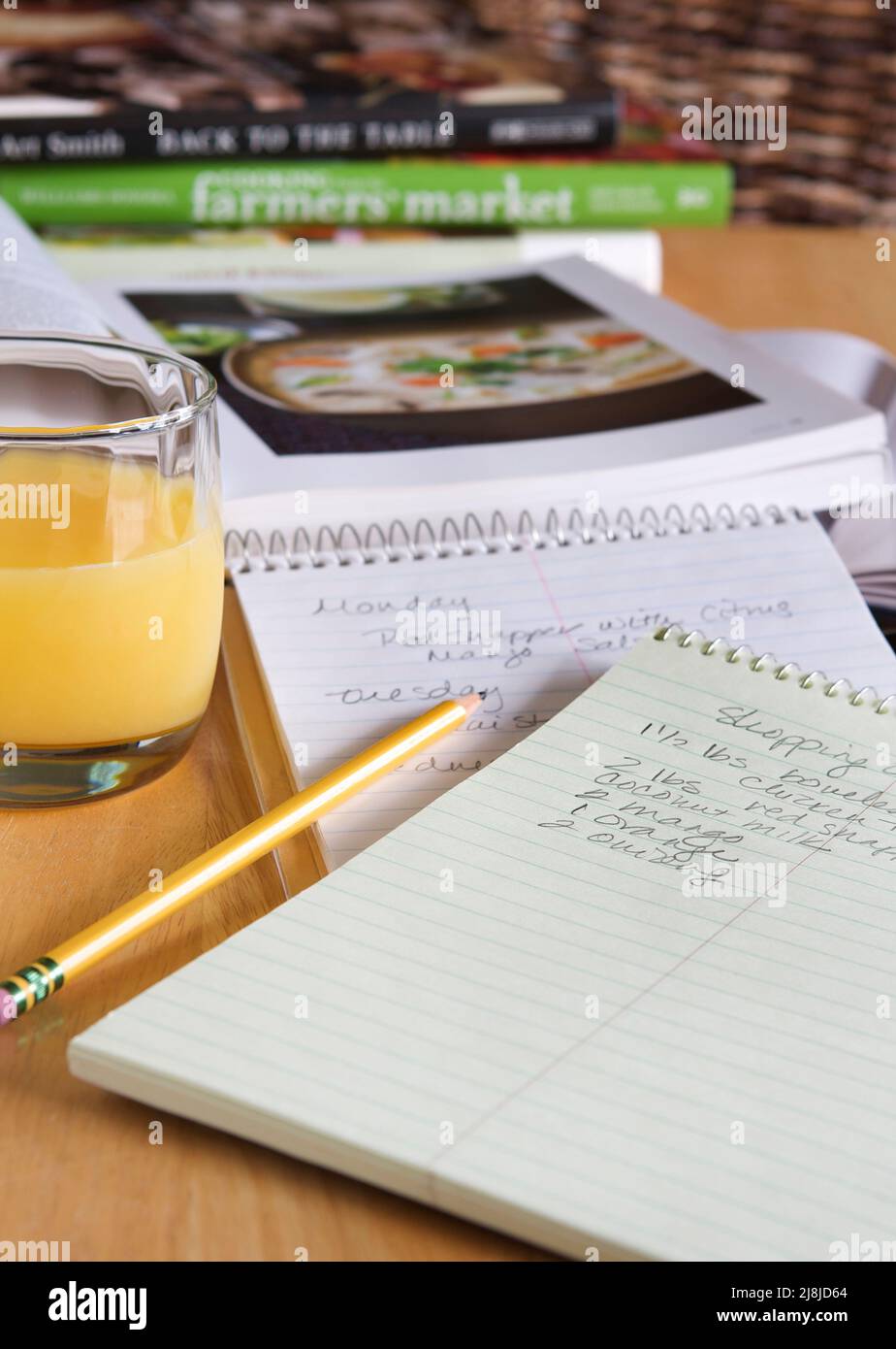 Einkaufsliste, Menüplaner und Kochbücher auf einem Holztisch mit einem Glas Orangensaft. Stockfoto