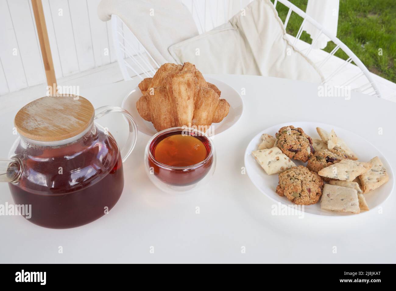 Sonntagsfrühstück im Hinterhof der Hütte. Frische süße Croissants mit Keksen auf dem Tisch. Transparente Teekane aus Glas mit gebrühtem Tee. Hochwertige Fotos Stockfoto