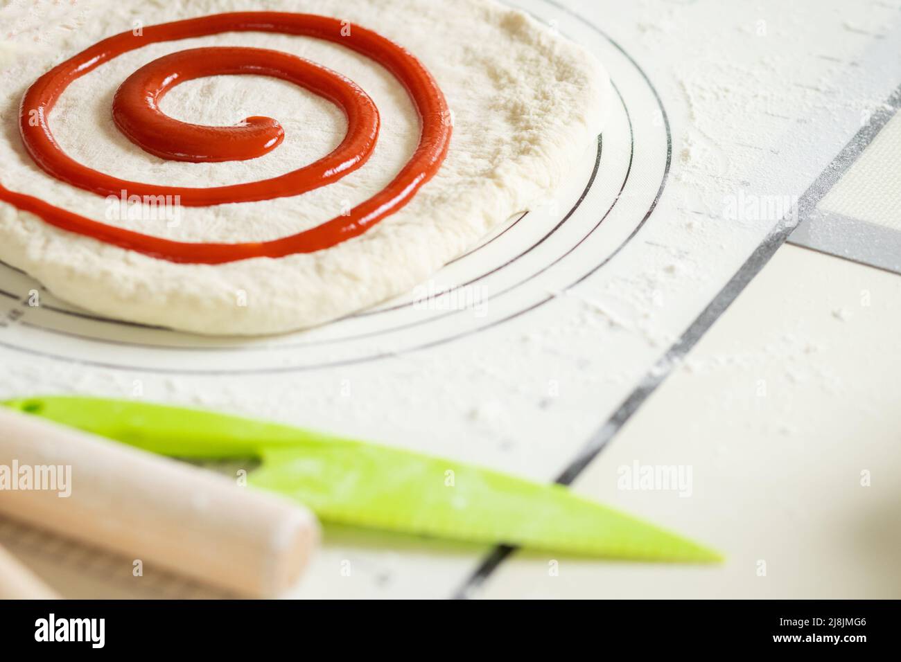 Beerenmarmelade spiralförmig auf den ausgerollten Teig aufgetragen, um eine süße Dessertrolle zu erhalten Stockfoto