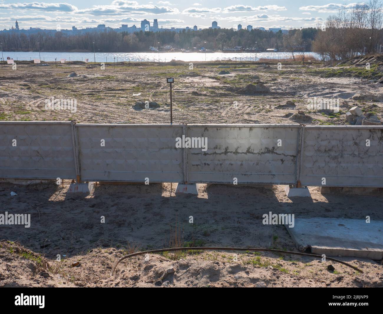 Der Panoramablick über die Baustelle hinter dem Betonzaun am Ufer des Flusses Dnipro und das rechte Ufer von Kiew am Horizont. Stockfoto