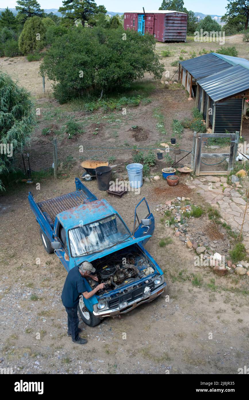Ein älterer Mann arbeitet am Motor seines alten blauen Pickup-Trucks, die Motorhaube angehoben, von oben geschossen, Lumberton, New Mexico, USA. Stockfoto