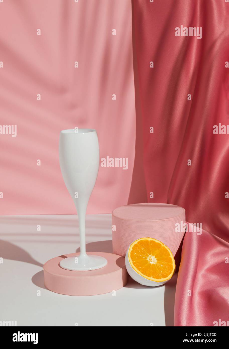 Weinglas mit frischen orangen Früchten, tropischem Palmenblatt-Schatten und Podium auf pastellrosa Hintergrund. Sommergetränk Minimales Konzept. Geeignet für Produkt Stockfoto