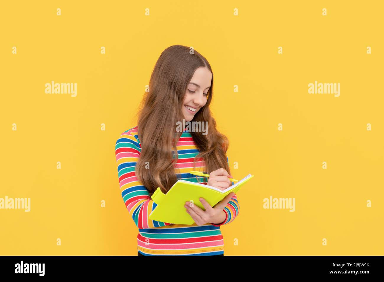 Glückliches Mädchen Kind schreiben in Copybook gelben Hintergrund, Alphabetisierung Stockfoto