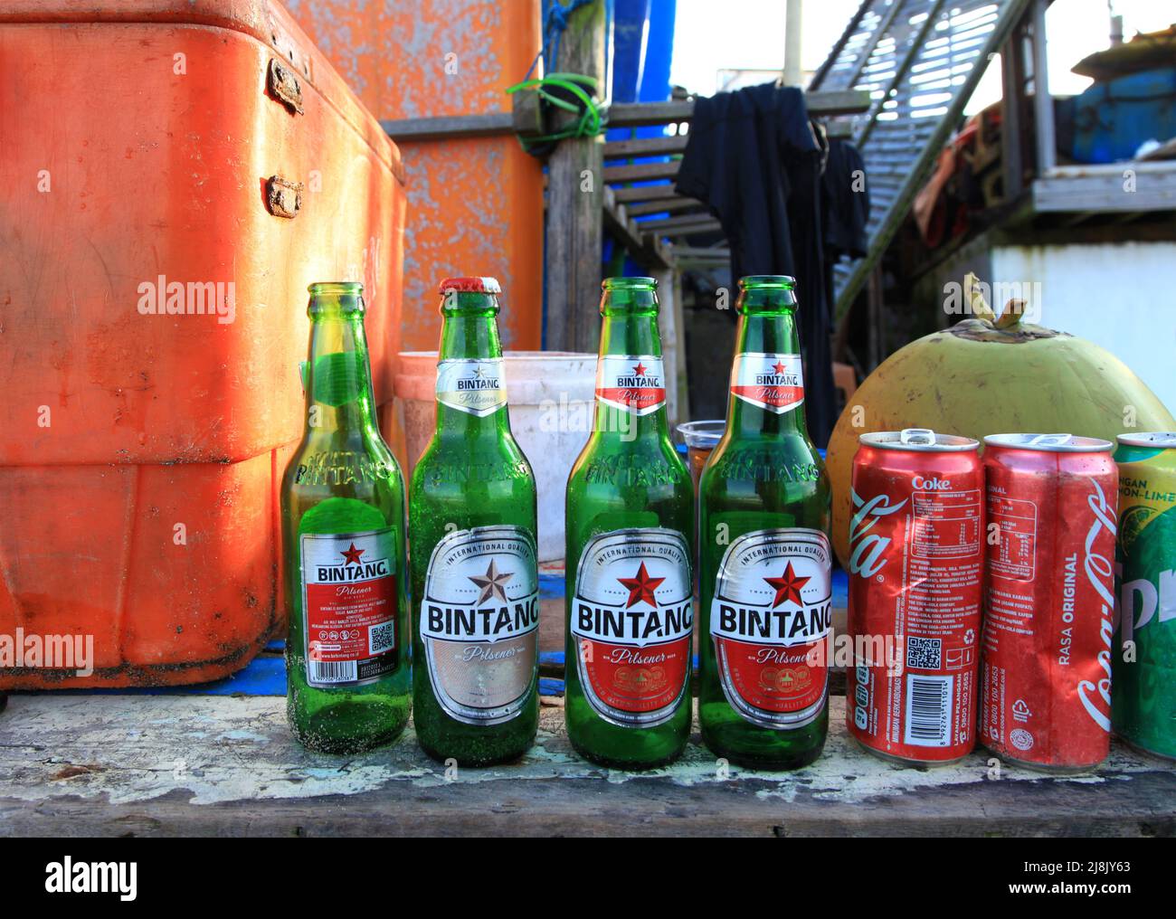 Eine Strandbar in Canggu, Bali, Indonesien, mit einer orangefarbenen Kühlbox und mehreren Leergut, darunter einheimische Biere Bintang, Coca Cola und Sprite Dosen. Stockfoto