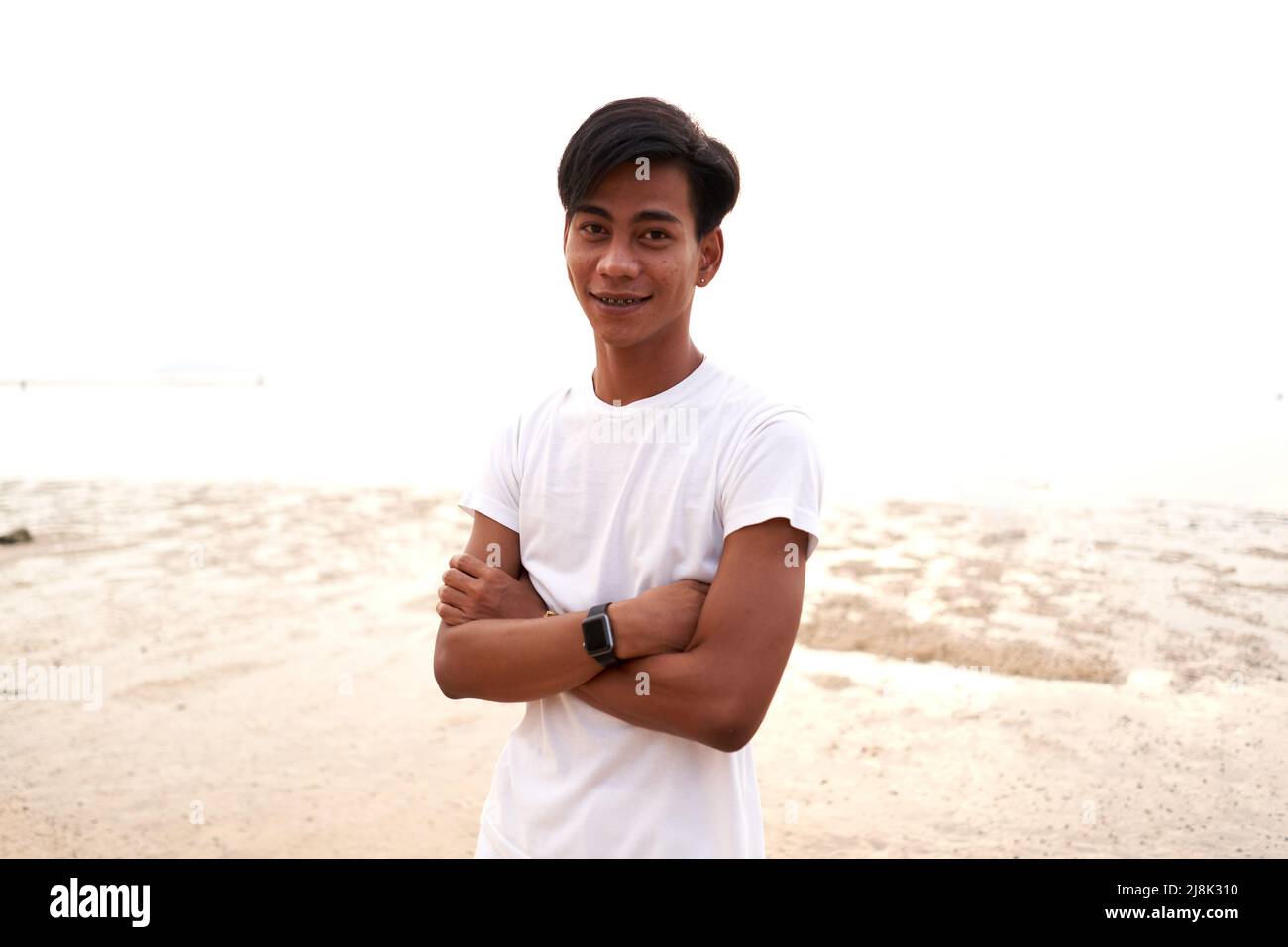 Asiatischer junger Mann mit gekreuzten Armen und digitalem Bazelet am Strand Stockfoto