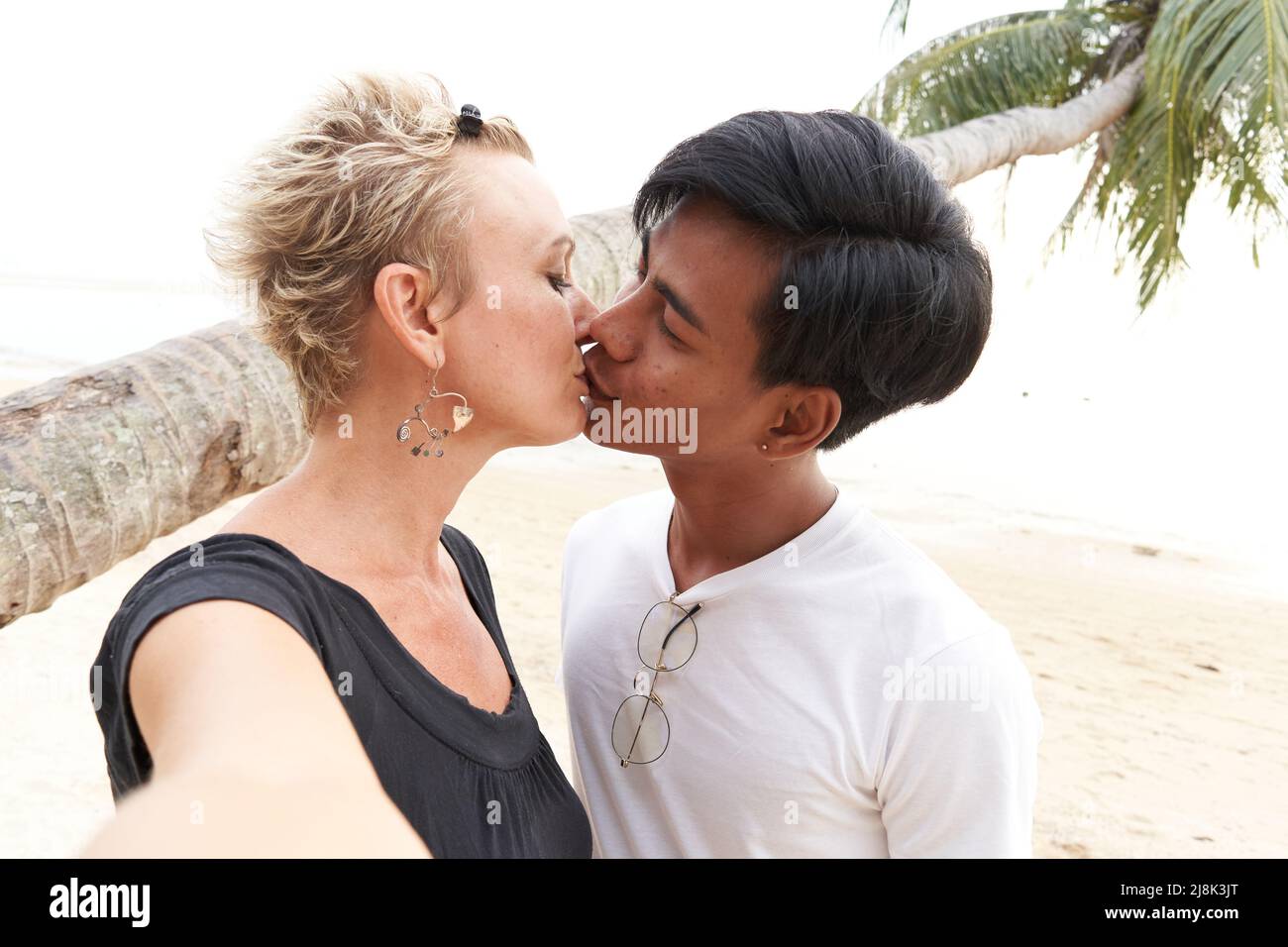 Multirassische Liebhaber küssen sich und machen ein Selfie am Strand Stockfoto