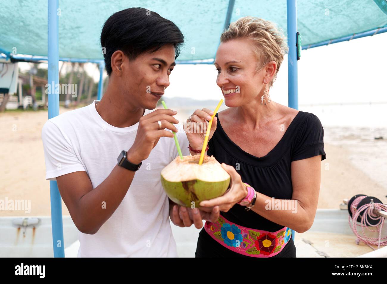 Ein Paar schaut sich an, während es eine natürliche Kokosnuss teilt, um am Strand zu trinken Stockfoto