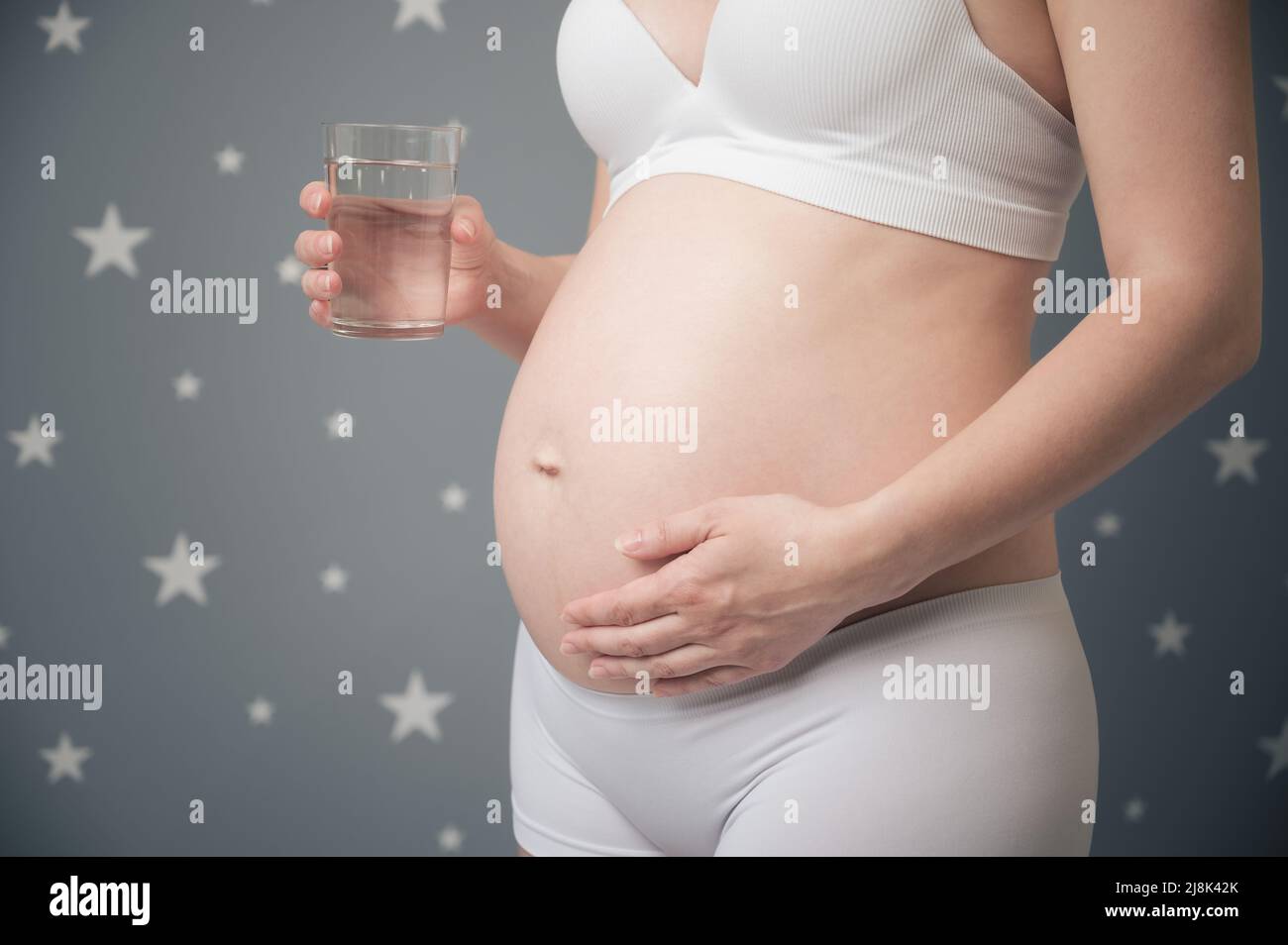 Schwanger Frau hält Glas mit Trinkwasser. Unerkannte, schwanger weibliche zärtlich berühren Bauch zu Hause. Gesundes Mutterschaftskonzept. Stockfoto