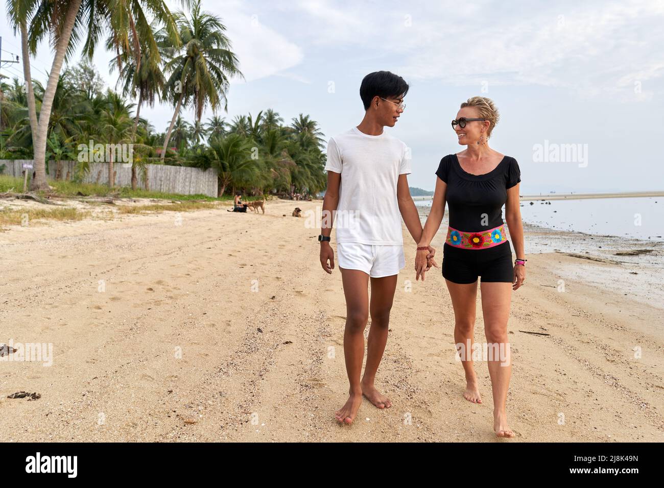 Multiethnisches Paar, das sich die Hände hält und an einem Sandstrand entlang läuft Stockfoto