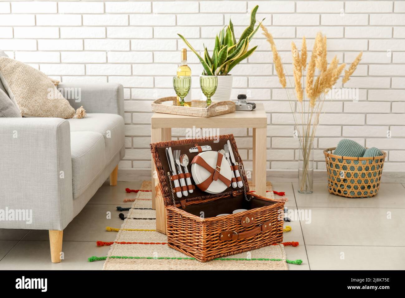 Korbkorb mit Geschirr für Picknick auf Teppich im Wohnzimmer Stockfoto
