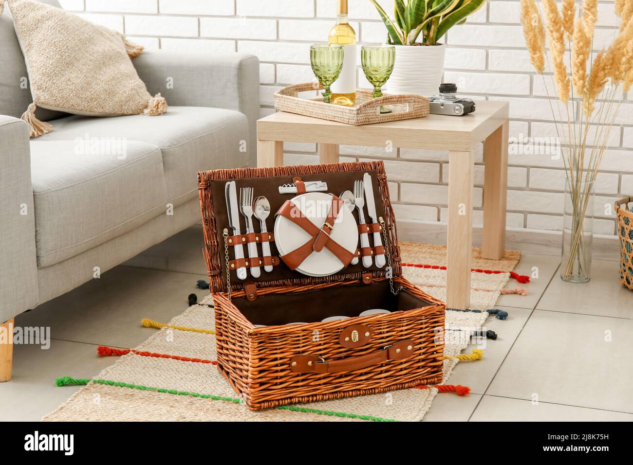 Korbkorb mit Geschirr für Picknick auf Teppich im Wohnzimmer Stockfoto