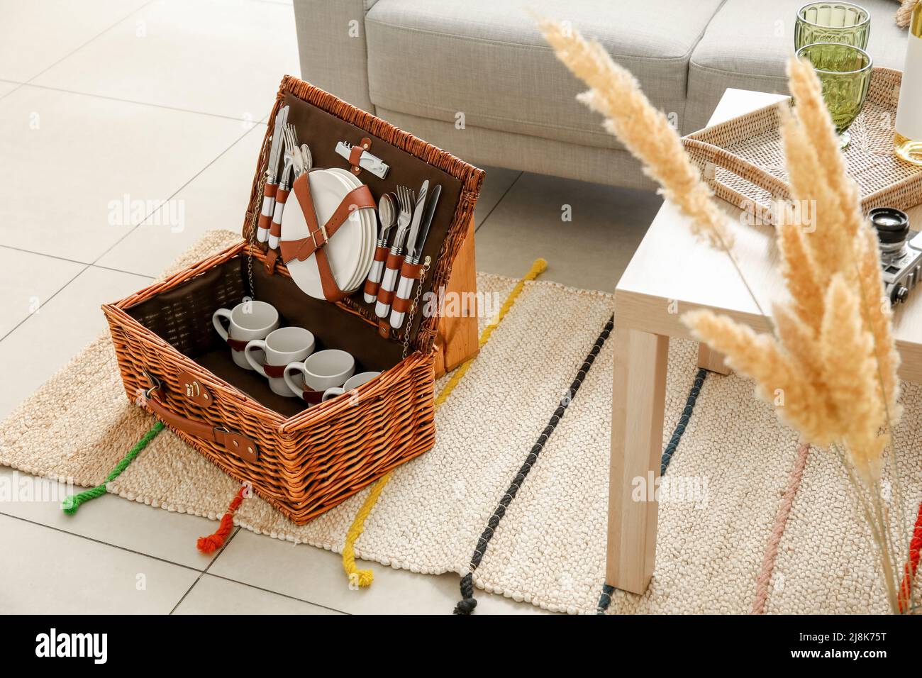 Korbkorb mit Geschirr für Picknick auf Teppich im Wohnzimmer Stockfoto