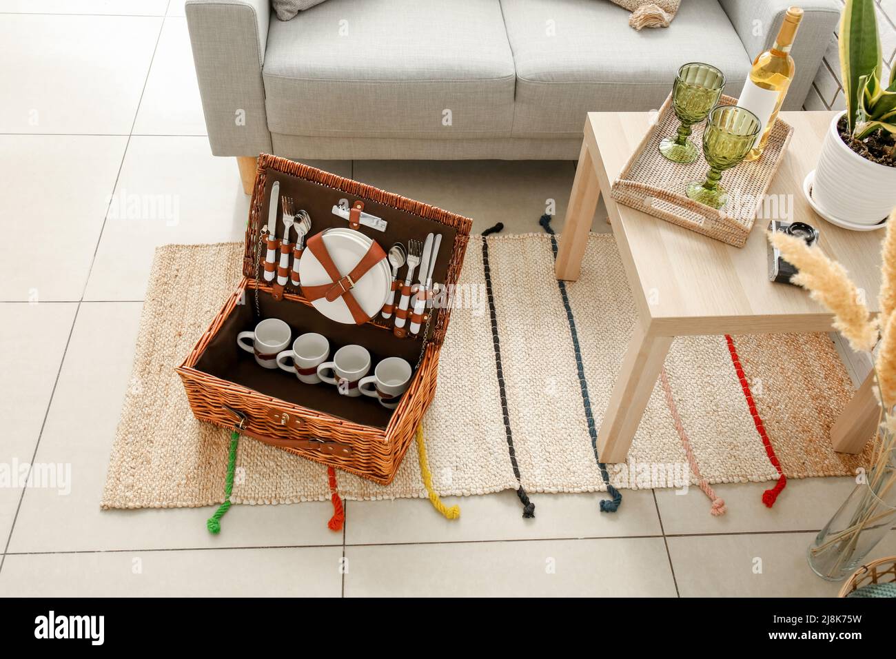 Korbkorb mit Geschirr für Picknick auf Teppich im Wohnzimmer Stockfoto