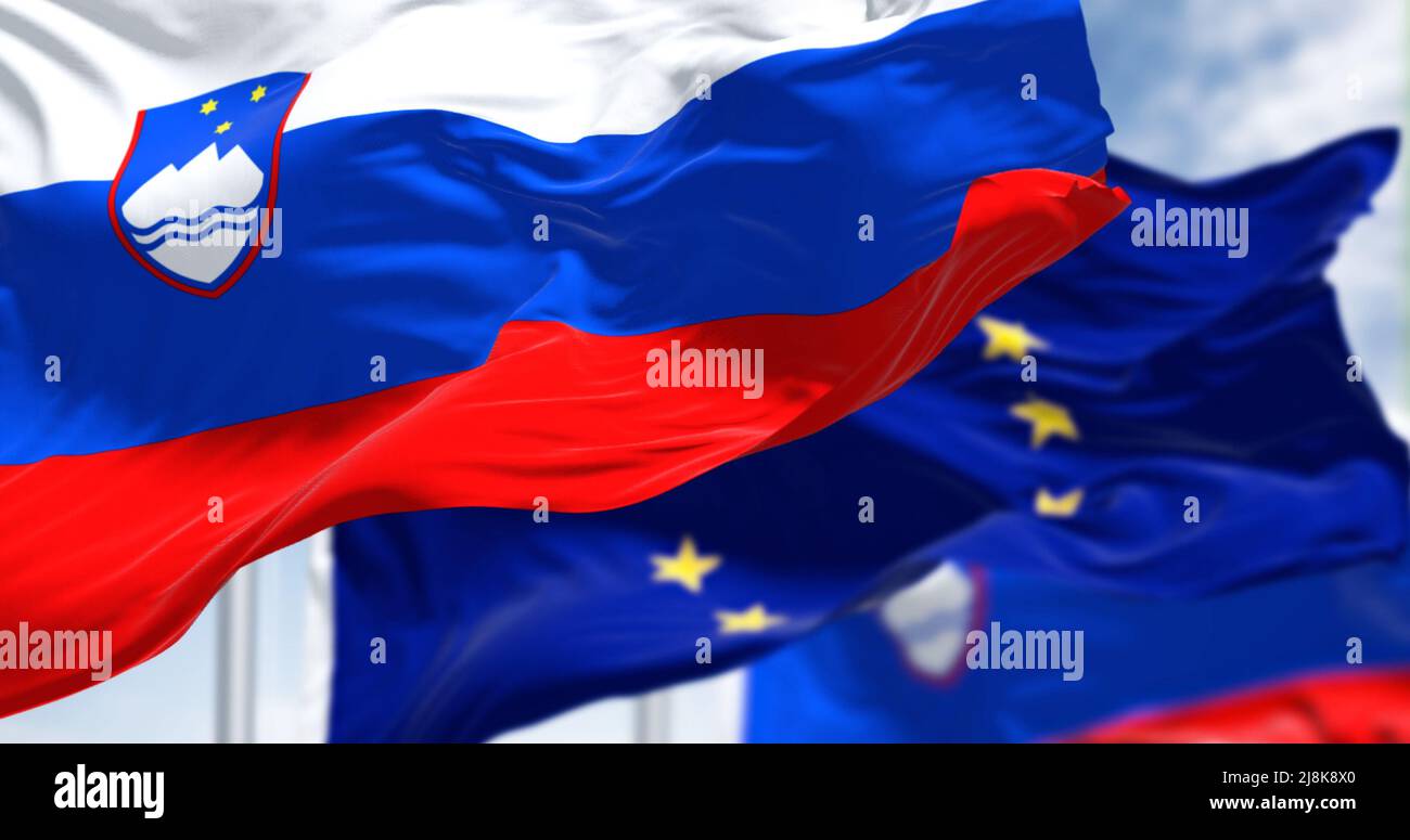 Detail der im Wind winkenden Nationalflagge Sloweniens mit verschwommener eu-Flagge im Hintergrund an einem klaren Tag. Demokratie und Politik. Stockfoto