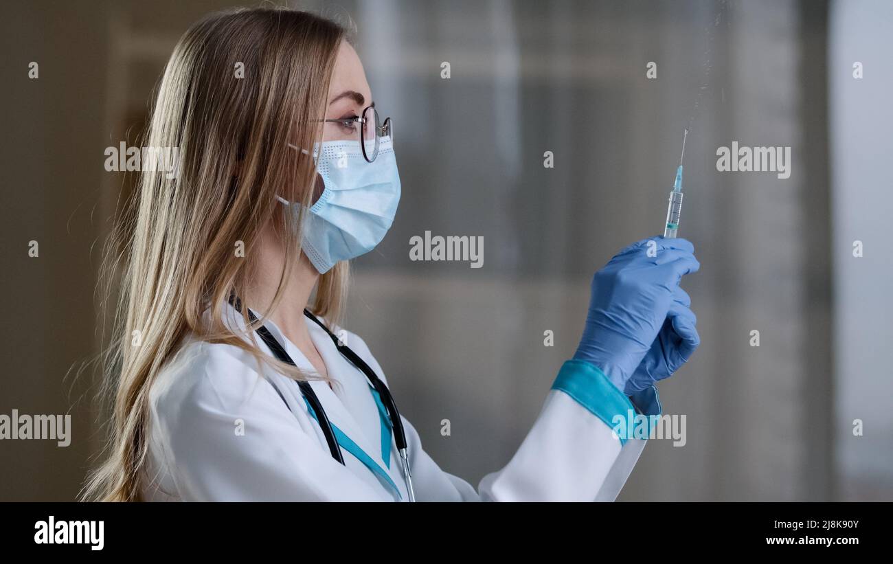Ärztin trägt eine Gesichtsmaske und einen medizinischen Kittel, der eine Spritze für die Injektion vorbereitet covid19 Impfung. Krankenschwester mit flüssiger Medizin Stockfoto