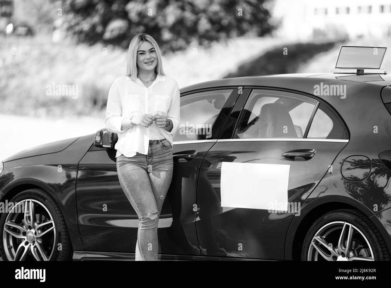 Glückliche Frau Instruktor Leaning auf ihrem Auto - vermutlich hat sie eine Pause vom Fahren Stockfoto